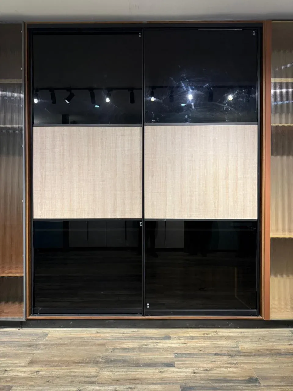 Sliding wardrobe combining black glass and light wood panels